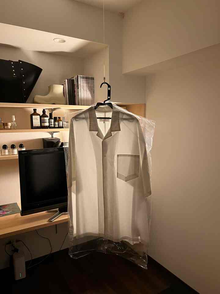 白と木目調の調和が取れた6畳のワンルーム、透明な洋服カバーに包まれたシャツとテレビ台があるミニマルな印象の空間