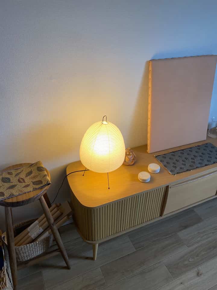 A warm beige-toned wall and light brown wooden furniture space featuring a low table lamp creating a soft, cozy ambiance