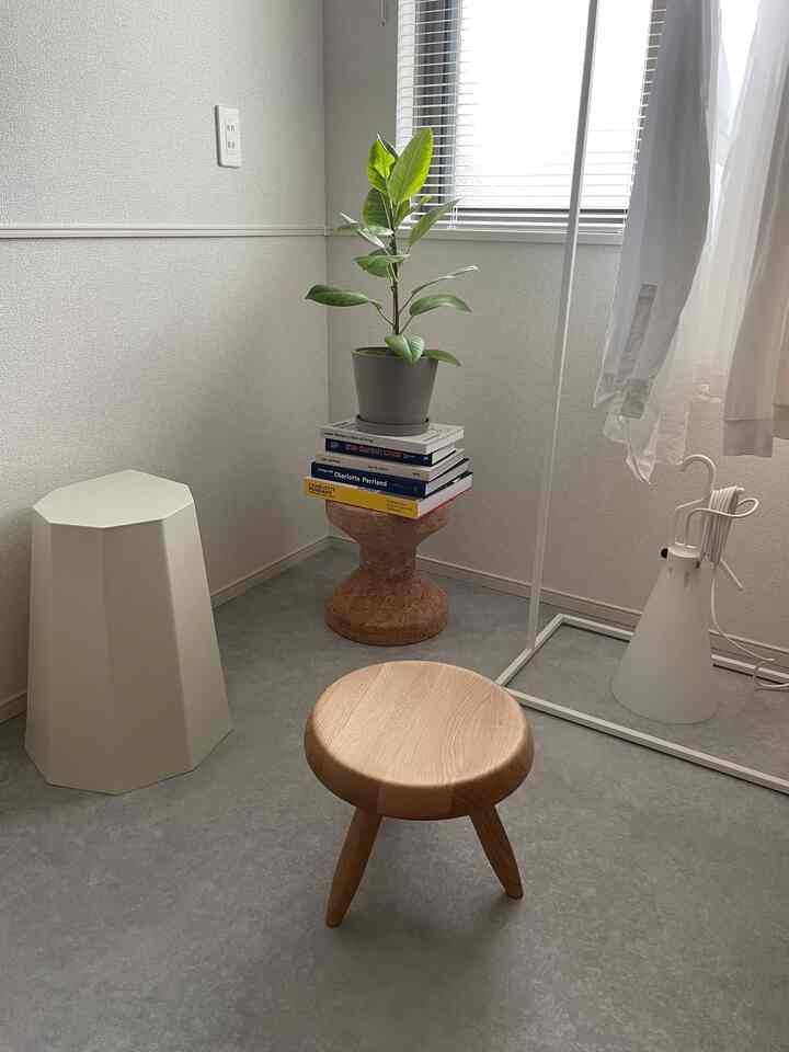 ホワイトとナチュラルトーンが支配的な小さな部屋、木製スツールとコルクのサイドテーブル、植物が配置された雰囲気のあるインテリア