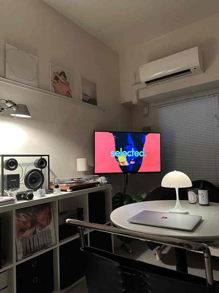 White-toned living room and home office space with round table featuring a table lamp and laptop, showcasing a clean interior