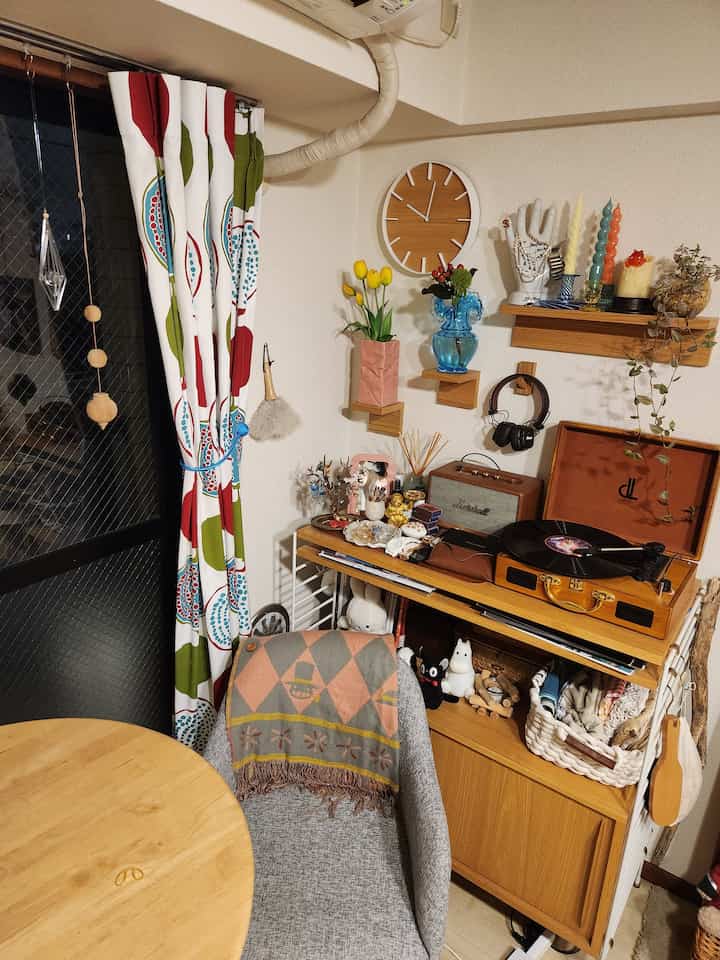 ウッドトーンとグレーの色調のリビング、柄付きカーテンと花瓶、壁掛け時計、ターンテーブルが配置された雰囲気のあるインテリア