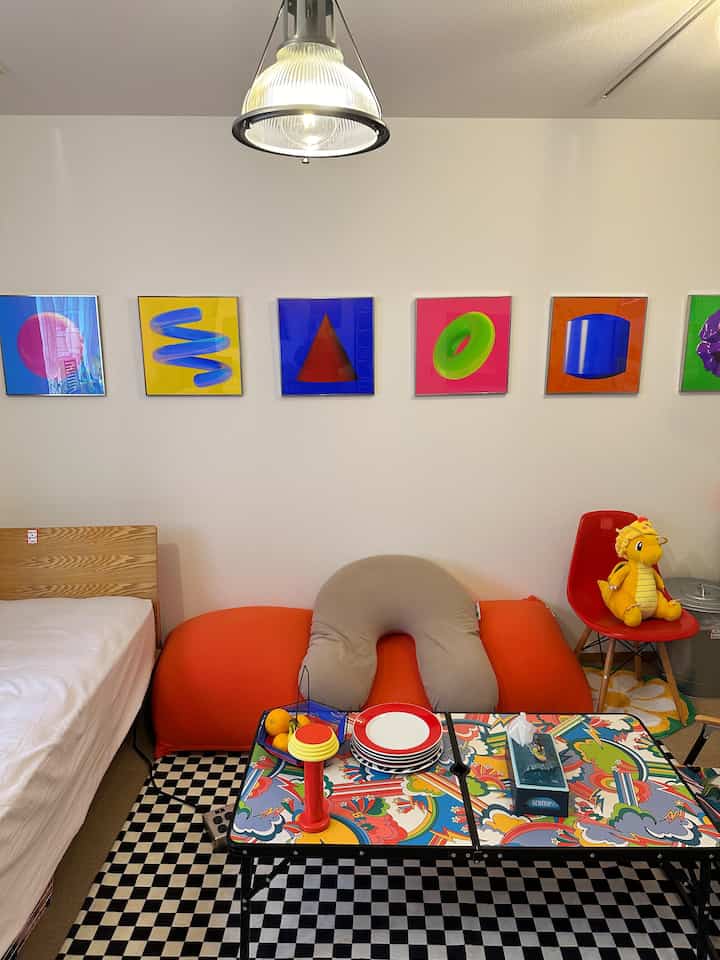Bright and cozy small bedroom featuring an orange bean bag sofa, colorful coffee table, and abstract framed art on the wall