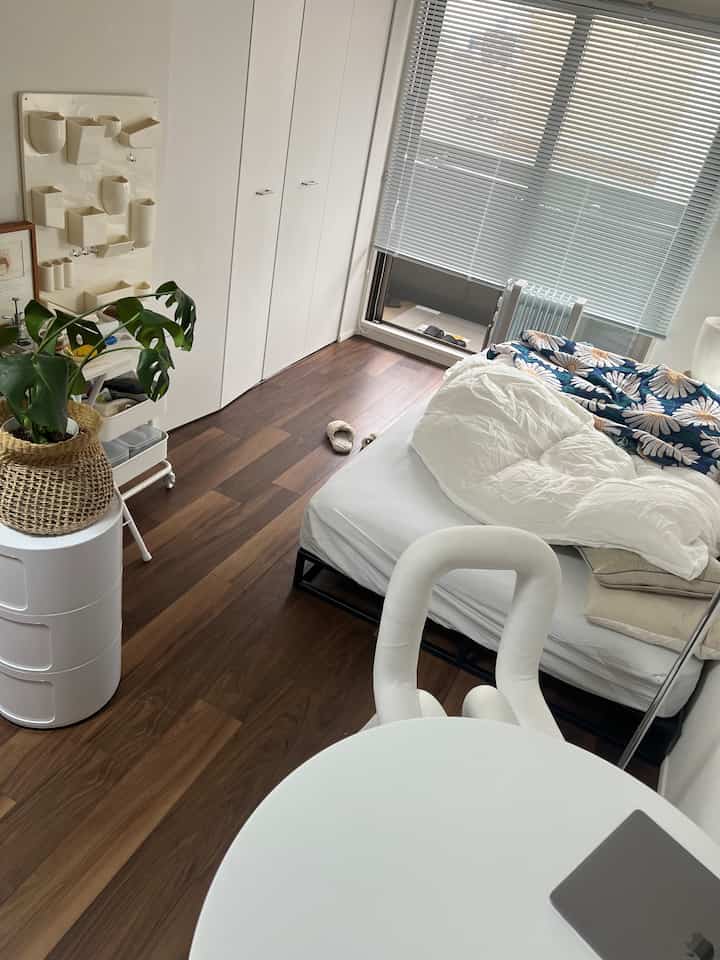 Small bedroom in white and wood tones featuring a neat bed, round table, and a plant creating a natural atmosphere