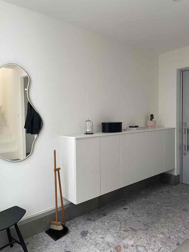 A clean entrance space with white walls and shoe cabinet, featuring a uniquely shaped pond mirror and gray tiled floor in modern style