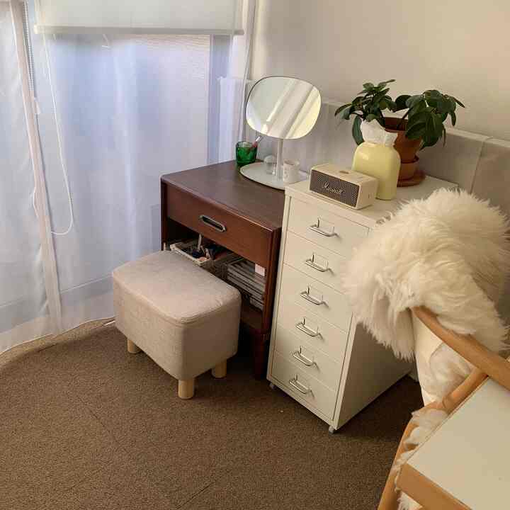 Small cozy window-side space in white and brown tones featuring a dark wood dresser, white drawer unit, and beige stool