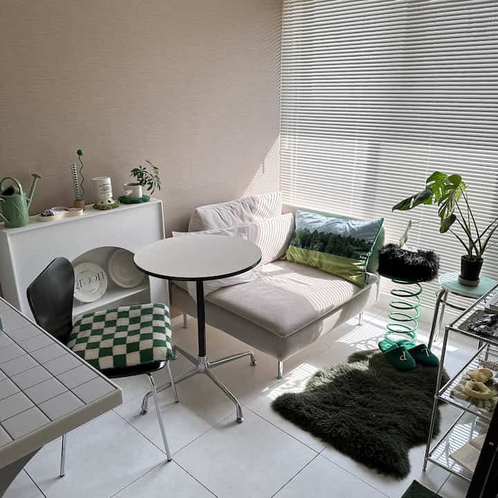 ベージュ色の壁と白いソファが配置された狭いリビング、緑のクッションと植物が調和した温かみのあるインテリア