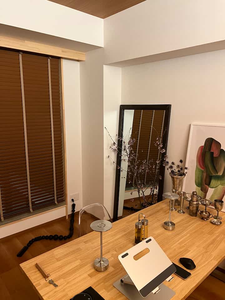 温かみのあるブラウンとホワイトのトーンのダイニングルーム、木製のテーブル上にノートパソコンスタンドとテーブルランプ、大きな鏡が配置されたモダンで自然な雰囲気のインテリア