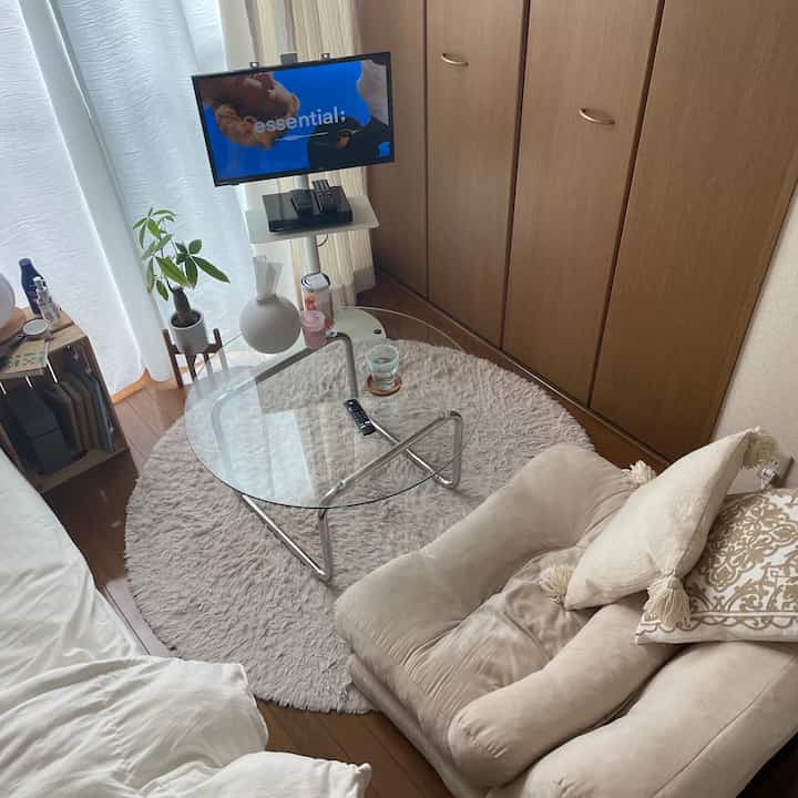 Beige toned studio living room featuring a sofa bed and a transparent round glass coffee table creating a cozy atmosphere