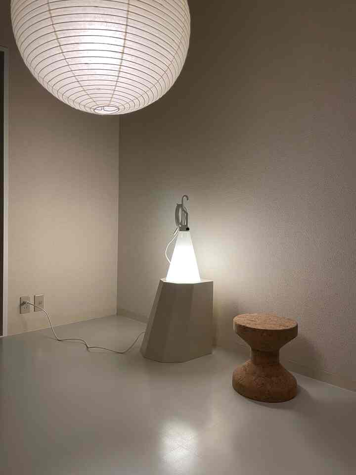 ナチュラルカラーの小さな部屋、コルクスツールと個性的なフロアランプが置かれたシンプルなインテリア