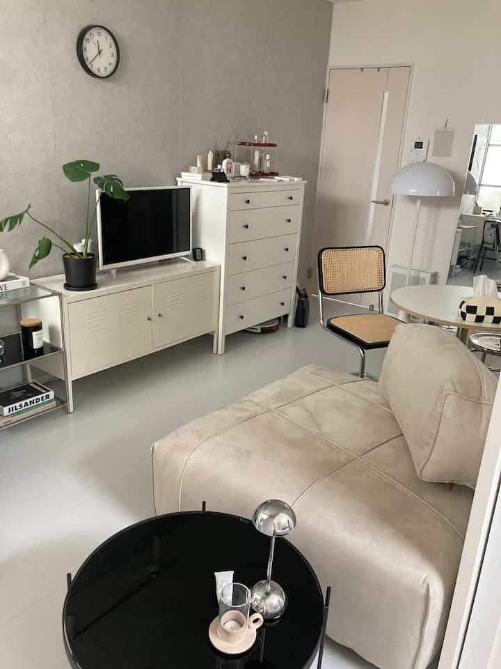 白とナチュラルな色調のリビング、ベージュの一人掛けソファとラタンチェア、黒い丸いサイドテーブルが配置された清潔感ある空間