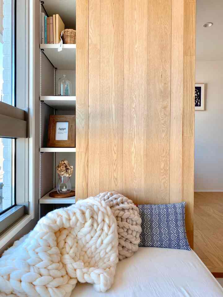 ベージュとホワイトの色調のリビングルーム、自然な木目の壁と柔らかな太いニットの毛布とクッションが配置された雰囲気のある空間