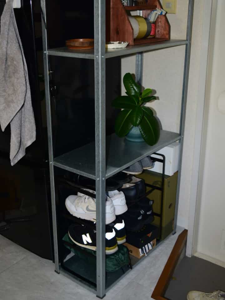 明るいグレーの床とベージュの壁の玄関、メタル製の棚に靴や観葉植物が配置された雰囲気のあるインテリア