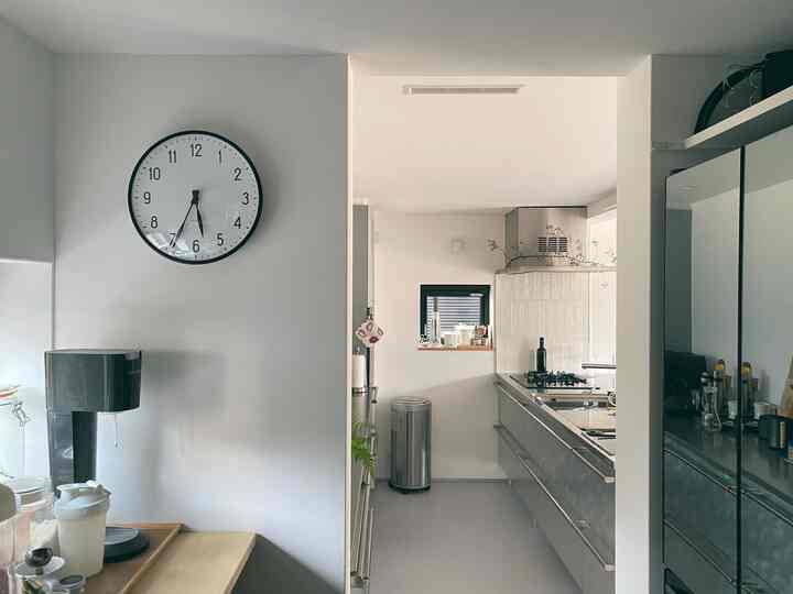 白とシルバーの色調が特徴的なキッチン空間、壁に時計が掛かり、冷蔵庫やソーダストリーム、自動ゴミ箱が配置されたミニマルでモダンな雰囲気のインテリア