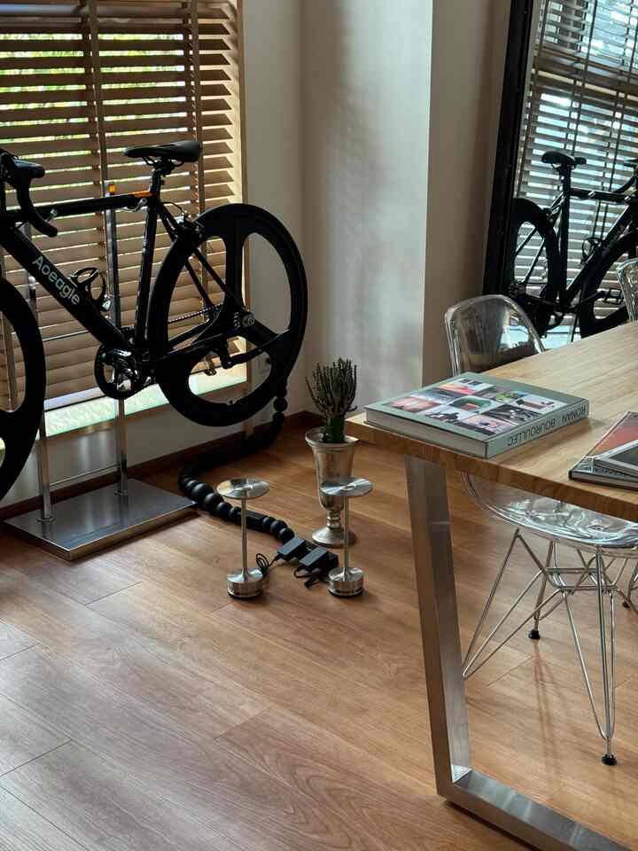 ナチュラルな木目調の床とモダンなテーブル、透明な椅子と自転車が配置された一人暮らしのリビング
