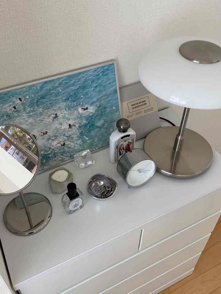 白とグレーのトーンのドレッサー上部にテーブルランプ、鏡、時計、香水などが配置されたミニマルで印象的な寝室の小物スペース