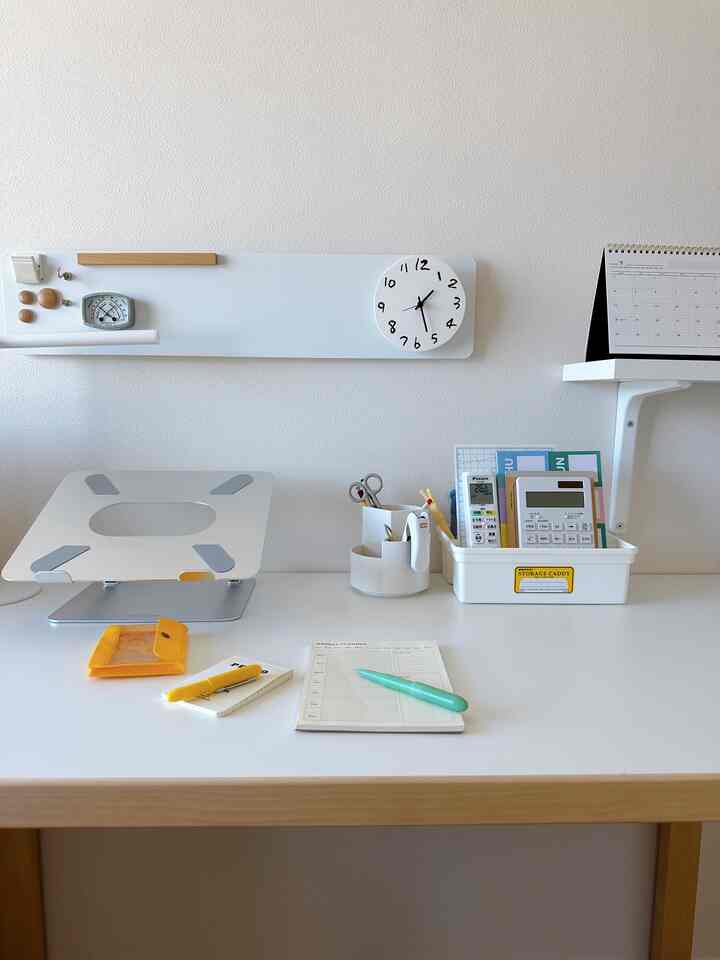 White and wood tone workspace featuring a simple desk with stationery and clock in a clean setting
