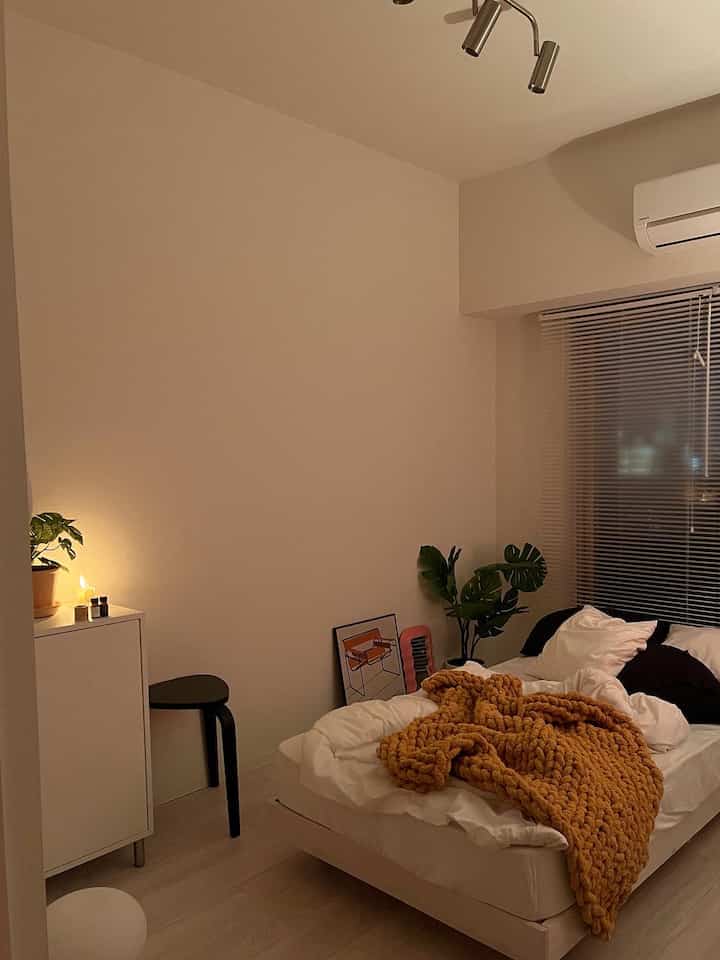 ベージュとホワイトの落ち着いた寝室、中央に大きなベッドと収納キャビネットが配置された雰囲気のあるインテリア