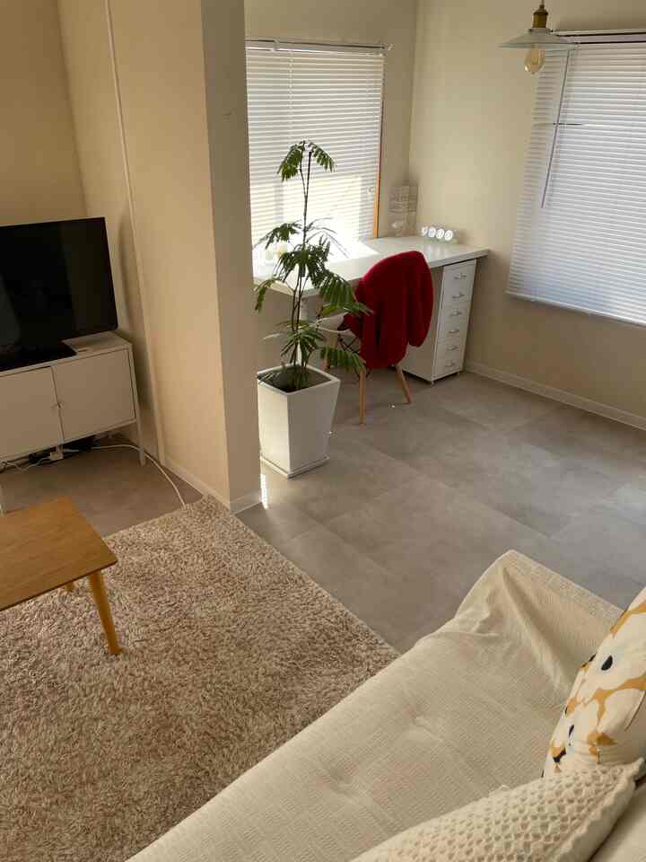 白とナチュラルカラーの明るいリビング、ソファとドレッサー、デスク、観葉植物が配置された雰囲気のあるインテリア