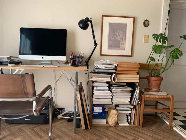 Natural-toned workspace featuring wooden desk, leather cantilever chair, stacked books, and a potted plant creating a cozy atmosphere