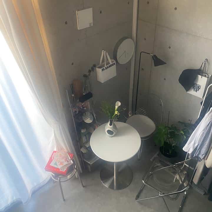 Small cafe style dining room in white and gray tones featuring a round dining table, metal chairs, floor lamp, and vase creating a modern minimal atmosphere