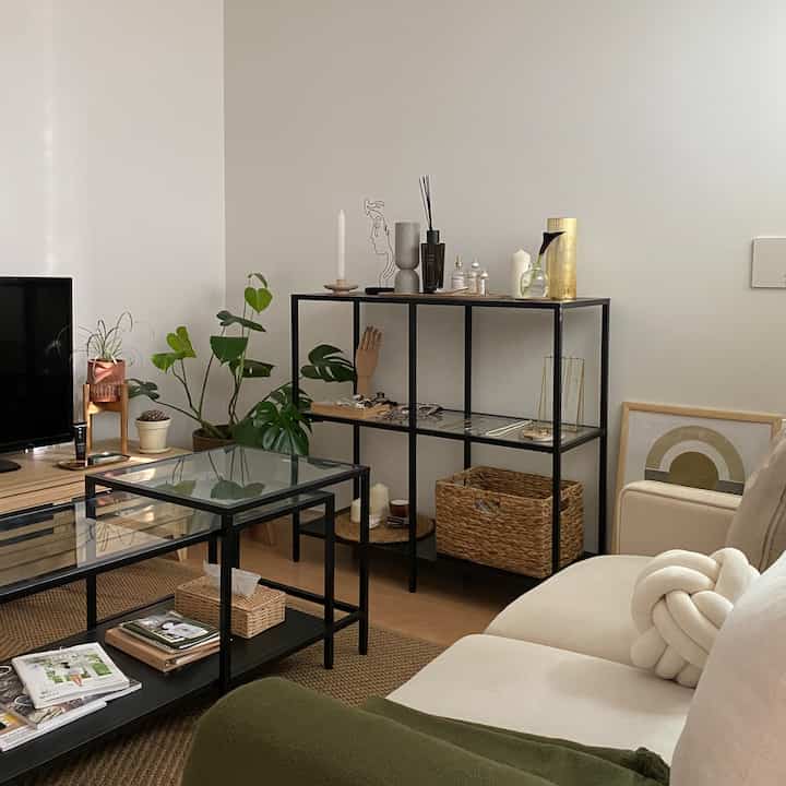 Beige sofa and black iron furniture in a natural-toned living room with green plants and organized storage, creating a cozy atmosphere