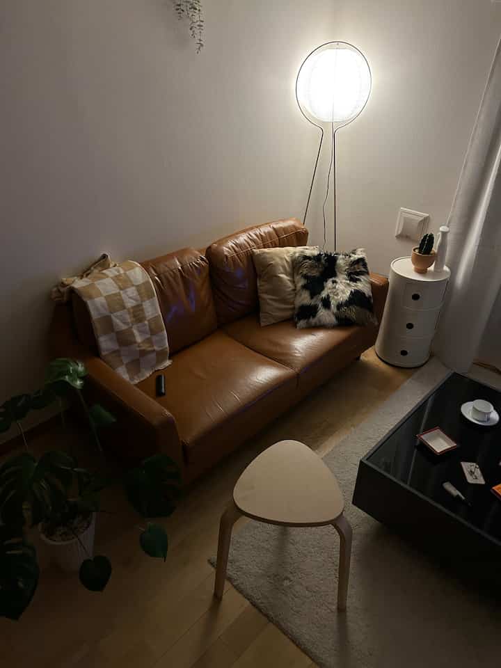 Cozy living room featuring dark brown leather sofa, wood tone flooring, and white floor lamp with warm ambiance