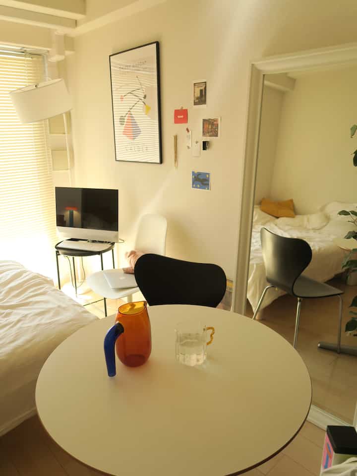 Light gray and white-toned studio apartment featuring a round table and modern chair in a cozy mid-century modern interior