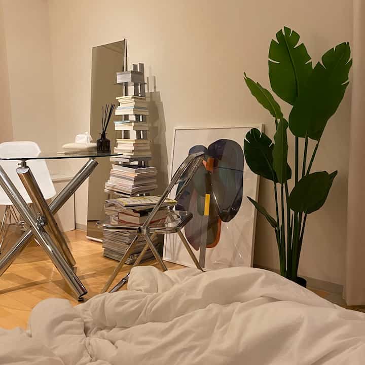 ナチュラルな色調のリビング空間、ガラスのダイニングテーブルと白い椅子、大きなフェイクグリーンが配置された雰囲気のあるインテリア