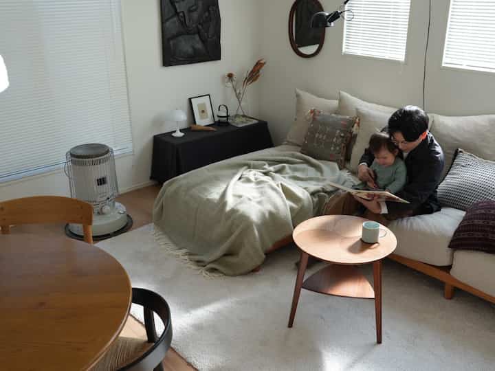 Natural-toned living room featuring a beige sofa and wooden table, with a father reading to a child on the sofa
