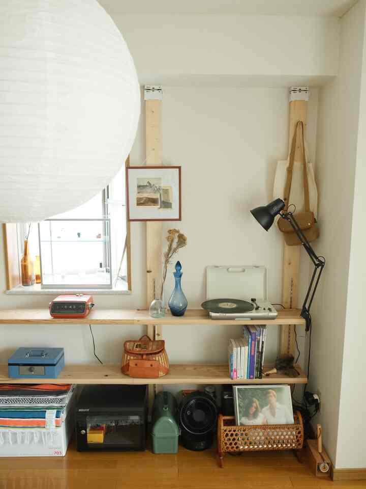 ナチュラルカラーとホワイトの色調の小さい部屋、木製の棚にレトロなレコードプレーヤーや多様なオブジェが配置された雰囲気のあるインテリア
