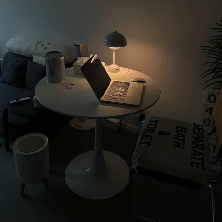 ホワイトとナチュラルトーンのワンルーム、ラウンドテーブルとテーブルランプが配置された雰囲気のあるホームオフィス空間