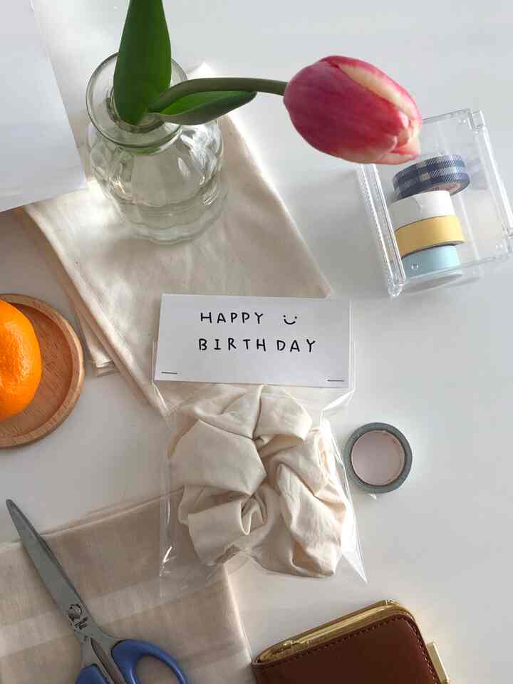 白を基調としたワンルームのデスクに透明な花瓶とベージュのテーブルクロス、はさみが配置された雰囲気のある作業スペース