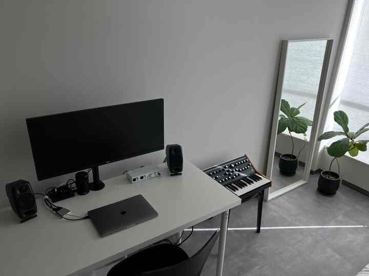 モノトーンの白とグレーのトーンが特徴的なホームオフィスのワークスペース、シンプルなデスクとモニター、緑の植物が配置された清潔感のあるインテリア