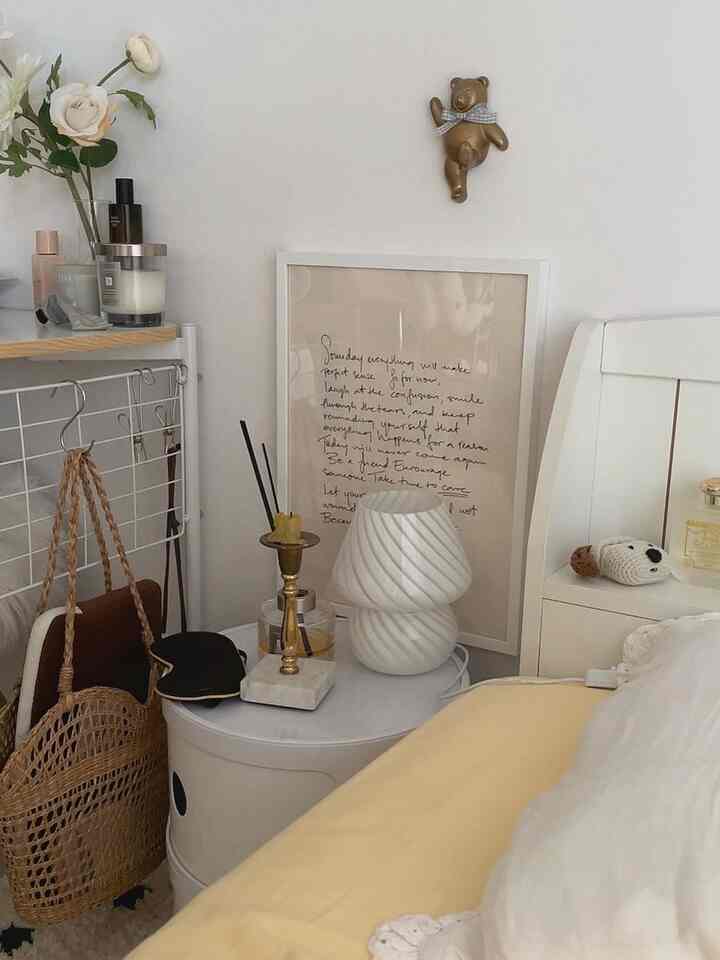 白とベージュの色調の寝室、ナイトテーブルの上にランプや装飾品が置かれたシンプルで自然な雰囲気のインテリア