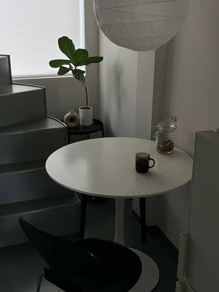 白と黒のトーンが特徴的なコンパクトなダイニング、ラウンドテーブルとアントチェアが配置されたシンプルなインテリア