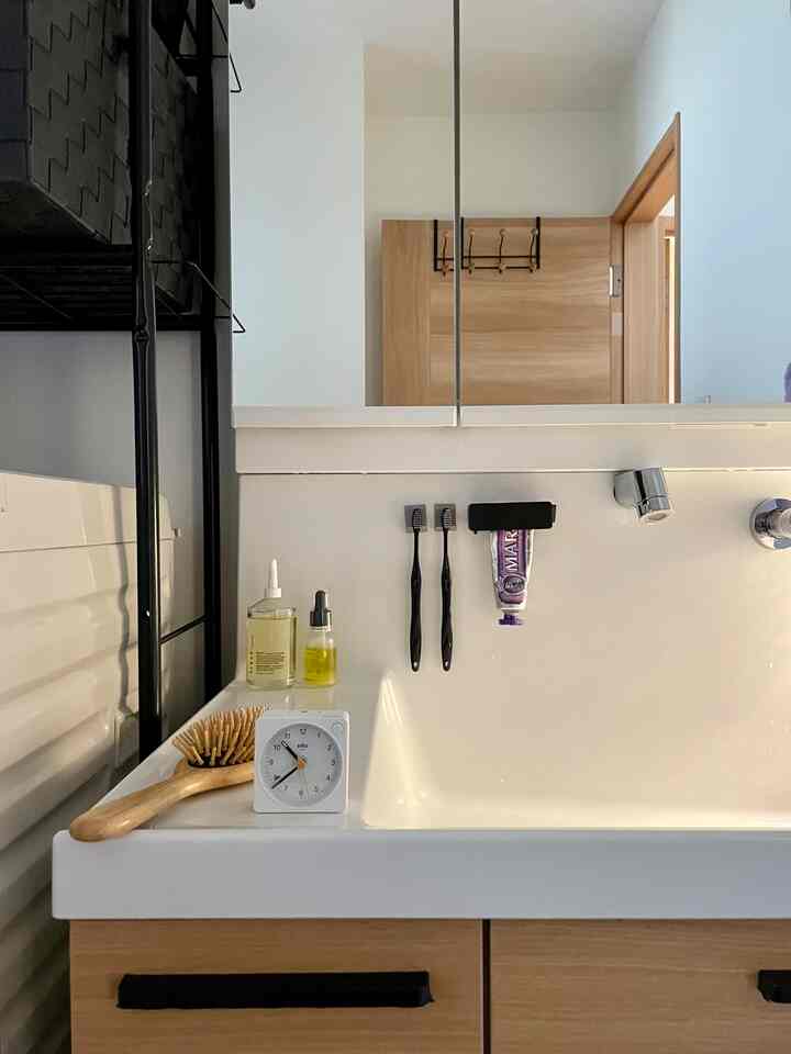 白と茶色のトーンが特徴のバスルームの洗面台、歯ブラシや時計、トイレタリーが配置された清潔感のある空間