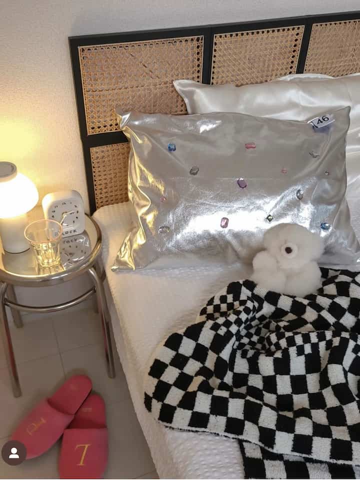 Cozy bedroom with beige rattan headboard, white bedding, silver cushion, and black-and-white checkered blanket