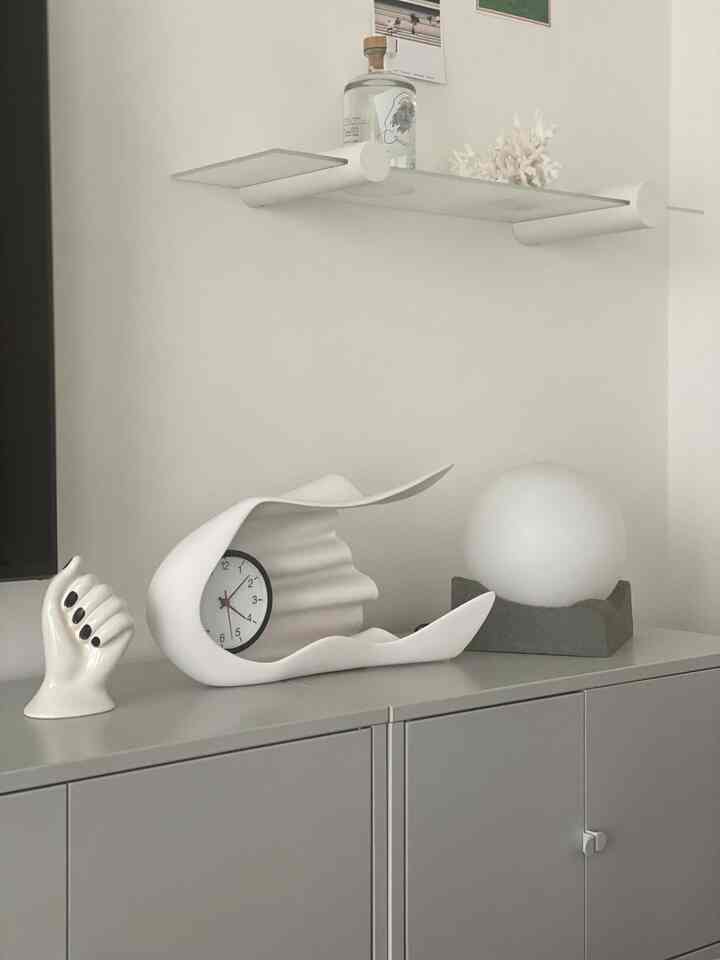 モノトーン調のリビングルーム、キャビネットの上に花瓶型の時計とテーブルランプが配置された印象的な空間