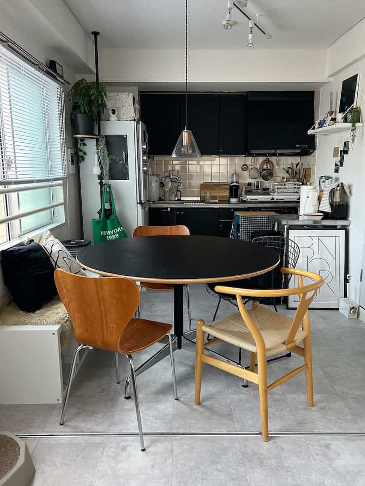 A compact dining room in black and natural tones featuring a round dining table and mixed chairs in a modern kitchen space