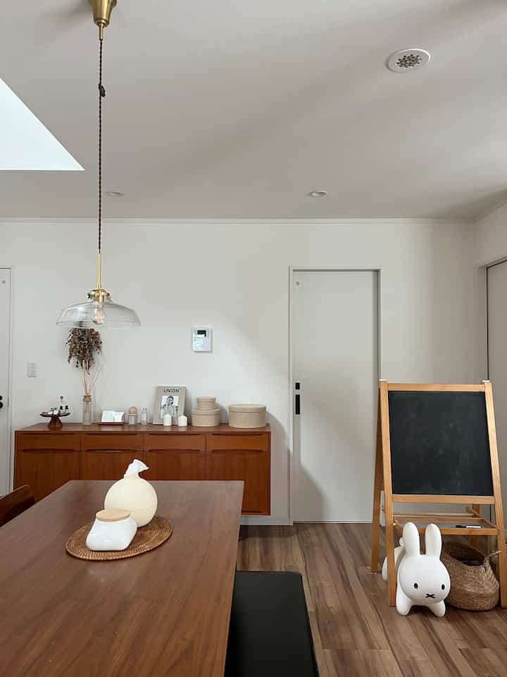 白い壁と木目調のダイニングテーブルとキャビネットが配置されたシンプルでナチュラルなダイニング、子供用のイーゼルとウサギの玩具もある空間