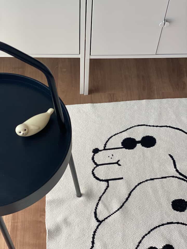 白と茶色のトーンの自然なインテリア、犬のキャラクターが描かれたラグと黒いIKEAのサイドテーブルが配置された空間