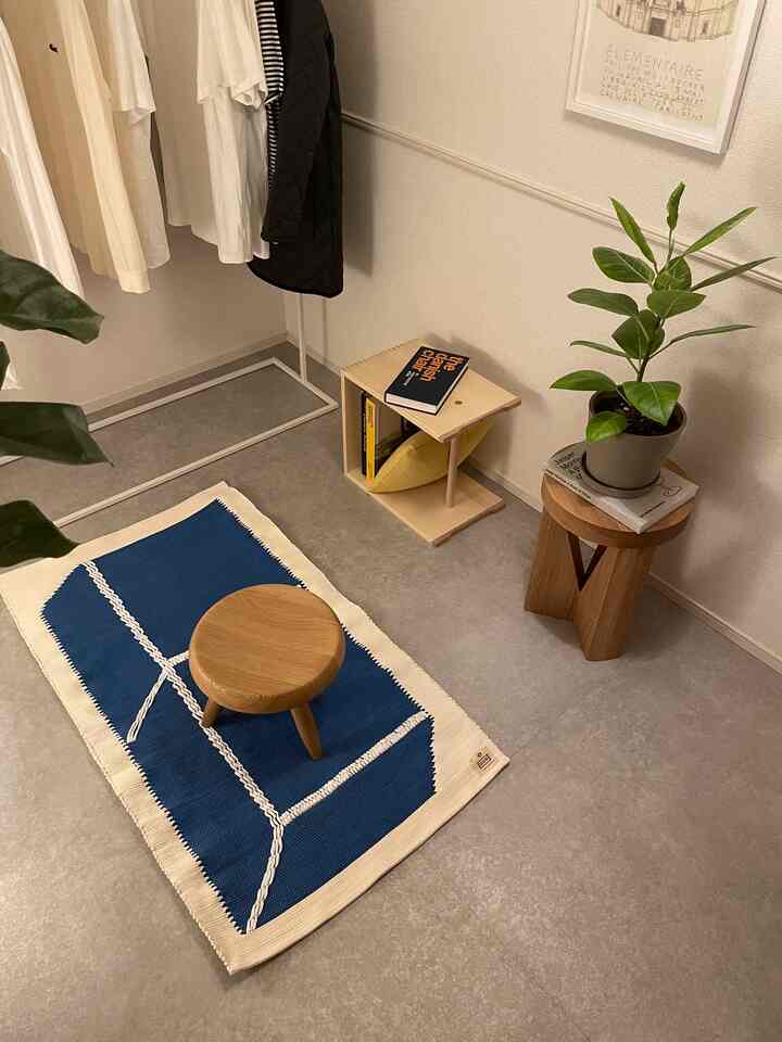 ネイビーと木目調の小さな部屋、スツールとコンパクトな本棚、観葉植物が配置されたミニマルなインテリア