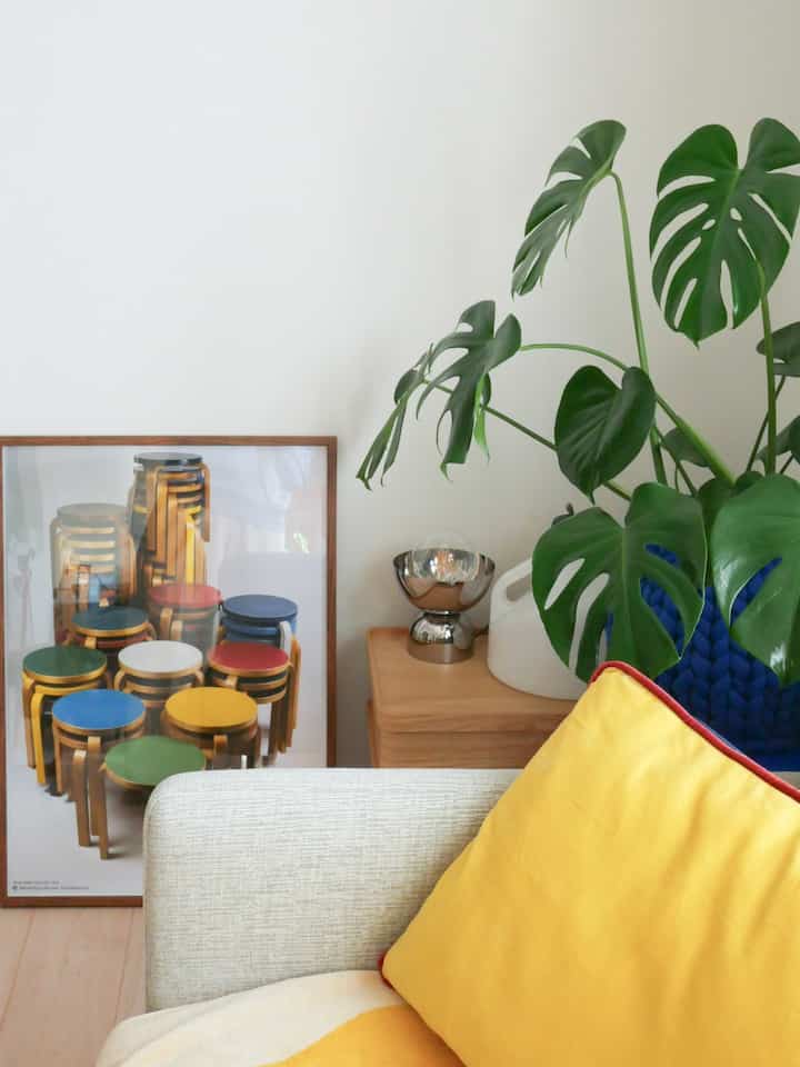 明るいアイボリーの壁とナチュラルな木目調家具が配されたリビング、黄色のクッションと大きな植物が印象的な雰囲気のあるインテリア