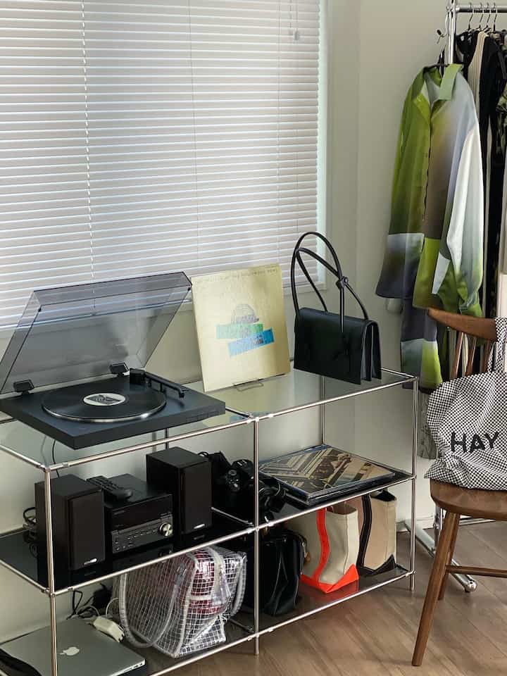 Compact living room featuring white blinds and a metal rack with audio equipment and various bags arranged