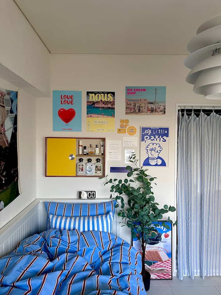 ブルーとホワイトの色調の寝室、ストライプの寝具とポスター、植物が配置された雰囲気のあるインテリア