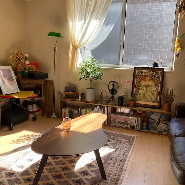 暖かいナチュラルカラーのリビング、木製のリビングテーブルと緑のフロアランプ、植物が配置された落ち着いた空間