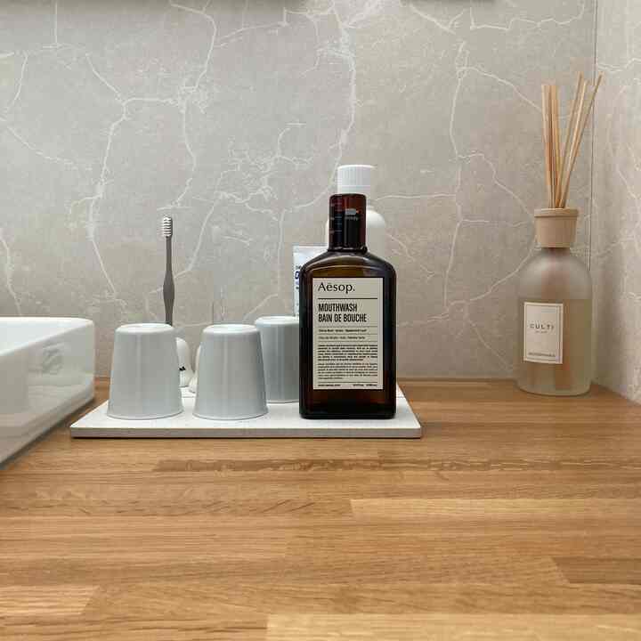 Natural toned bathroom countertop featuring a diffuser, mouthwash, toothbrush, and white cups with a clean minimalist style