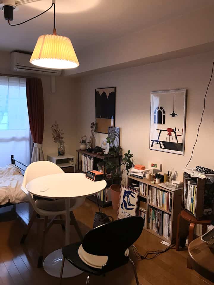 温かみのあるウッドトーンと白い家具が配置された一人暮らしの寝室兼ダイニング、ポスターや照明が雰囲気を醸し出す印象的なインテリア
