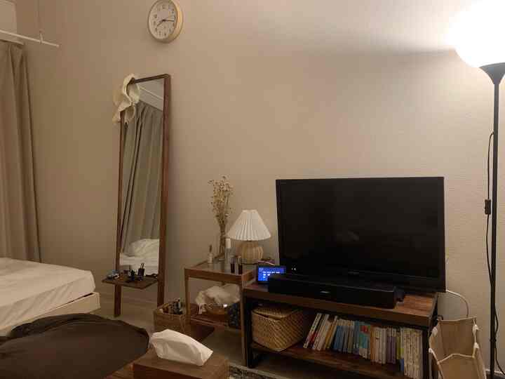 Cozy bedroom with white walls and wood tone furniture, featuring a full-length mirror and a TV setup