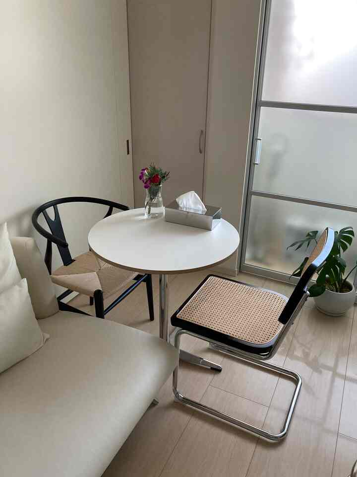 A cozy living room with white walls and natural wood floors featuring two rattan chairs and a small round white table near a frosted window